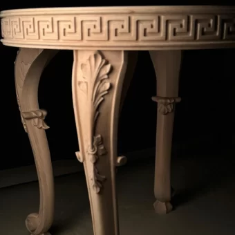 Close-up of a high-end wooden table leg and apron, featuring a carved Greek Key (meander) pattern along the rim and acanthus leaf scrolls on the curved legs. Luxury handcrafted wooden table with Greco-Roman inspired details and ornate sculpted legs.