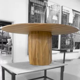 A modern circular dining table featuring a thick, natural wood grain top supported by a heavy, vertical-slat fluted pedestal base in a light-toned wood.
