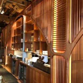 The finished interior of Bar Madrina in Toronto, featuring the installed geometric wood screen and warm integrated lighting, showcasing the final result of expert custom wood fabrication.