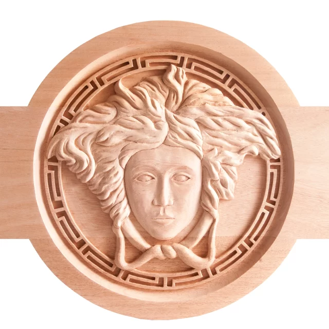 A circular wooden architectural element featuring a detailed 3D carving of the Versace Medusa head, framed by a classic Greek Key border.