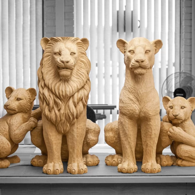 A proud collection of four wooden lion sculptures, including two large adults and two cubs, featuring highly detailed facial expressions and realistic mane textures.
