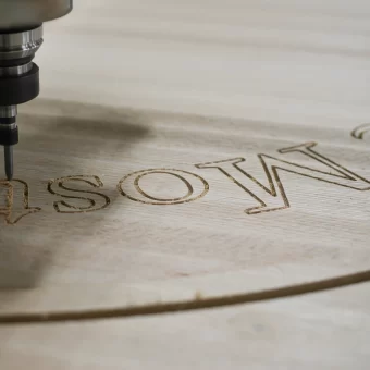 A close-up shot of a CNC machine precision-carving custom text into a wooden sign, showcasing the technological side of custom wood fabrication.