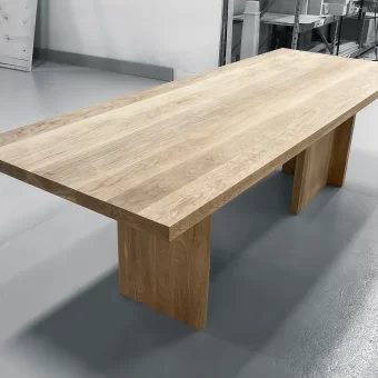 A large-scale executive office table showcasing premium custom wood fabrication with a thick, natural grain solid wood top and minimalist structural supports.