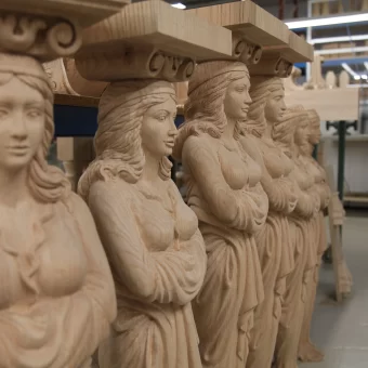 A row of several custom-carved wooden sculptures depicting the Venus de Milo, showcasing classical proportions and detailed drapery carved from light-colored timber.