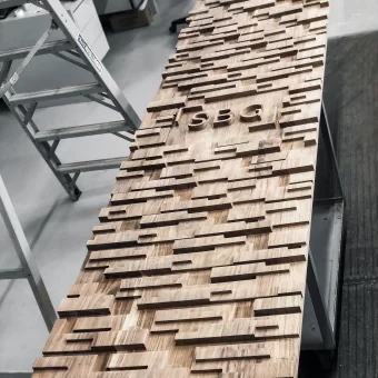 An artistic display of custom woodwork featuring a staggered 3D blocking pattern and recessed name signage, showcasing complex custom wood fabrication for a branded commercial interior.